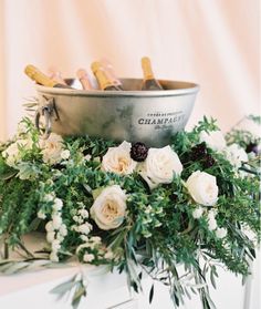 flowers and greenery are arranged in front of a silver bowl on top of a dresser