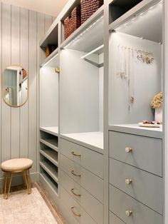 a walk - in closet with white drawers and gold hardware on the shelves, along with a stool