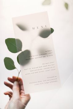 a person holding up a piece of paper with the word menu written on it and green leaves