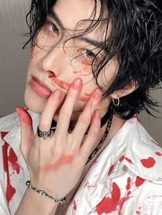 a man with black hair and red paint on his face, holding his hand up to his face