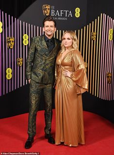 a man and woman standing on a red carpet in front of a black wall with gold stripes