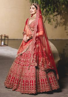 a woman in a red and gold bridal gown is walking down the street with her veil draped over her head