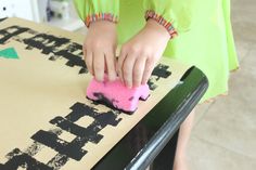 a child is playing with a pink object on top of a cardboard box