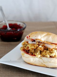 a sandwich on a plate next to a bowl of fruit and a spoon in the background