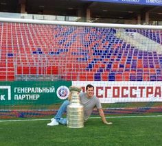 a man sitting on the ground next to a soccer trophy in front of a goal net