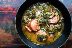 a black bowl filled with meat and vegetables on top of a wooden table next to a spoon