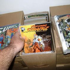 two boxes with comic books in them are being held by a man's hand