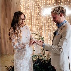 a bride and groom exchanging wedding rings in front of a string of lights on the wall