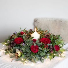 a bouquet of red roses and greenery with a lit candle on a white tablecloth