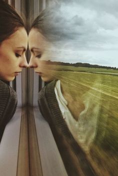 two women facing each other in front of a train window with grass and sky behind them