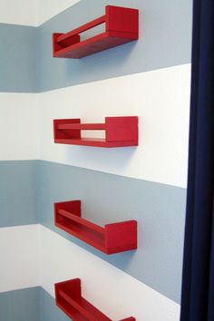 three red shelves on the wall in a room with blue and white striped walls behind them