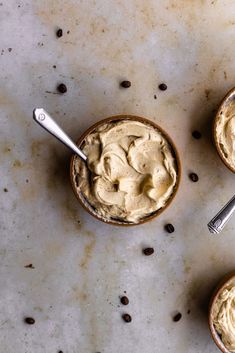 three small bowls filled with peanut butter on top of a marble counter next to two spoons