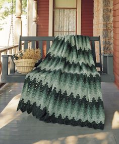 a crocheted blanket sitting on top of a wooden porch next to a bench