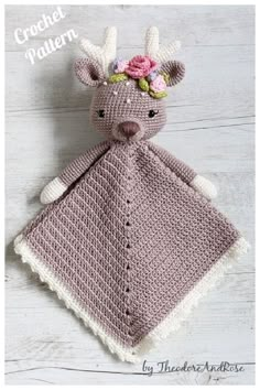 a crocheted deer blanket with flowers on it's head sits on a white wooden surface