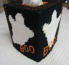 a close up of a knitted tissue box on a white table cloth with an orange and black design