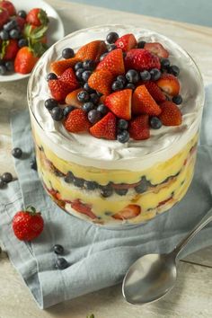 a dessert with strawberries and blueberries in it on a napkin next to two spoons