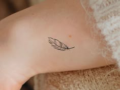 a woman's arm with a small feather tattoo on the left side of her arm