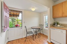 an empty kitchen and dining room with wood flooring, white walls, and wooden cabinets