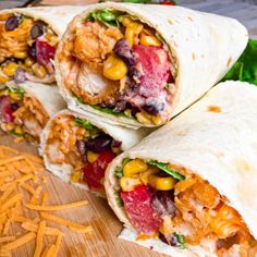 three burritos on a cutting board with shredded cheese and other ingredients in the background