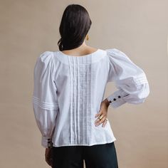 Extraordinary pintuck details on both the romantic puffed sleeves and the front and back of this blouse create a gorgeous statement piece. Billowy soft handwoven cotton and artisan-handicraft make for a piece that looks good and feels good. Sizing: This shirt runs large. We recommend ordering a size down. XS (US size 2-4) S (US size 6-8) M (US size 10-12) L (US size 14-16) Materials and Care: Handwoven cotton. We recommend dry-cleaning these garments or machine-wash cold with like colors. Hang t Feminine Fitted Cotton Peasant Top, Billowy Cotton Feminine Blouse, Billowy Cotton Blouse Feminine Style, Fitted Chic Cotton Peasant Top, Feminine Cotton Blouse With Smocked Cuffs, Fitted Feminine Cotton Peasant Top, Cotton Peasant Top With Puff Sleeves And Ruffles, Chic Fitted Cotton Peasant Top, Cotton Peasant Top With Ruffles And Puff Sleeves