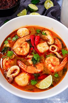 a white bowl filled with shrimp and red pepper soup on top of a blue table cloth