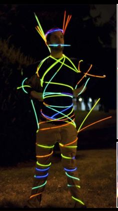 a man is standing in the grass with neon lights on his body and hands behind him