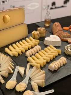 several different types of cheese are arranged on a black table with utensils and spoons