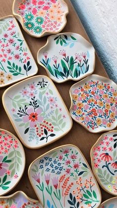 many plates with flowers painted on them sitting on a wooden table next to each other