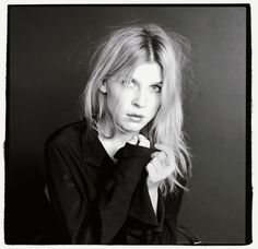 a black and white photo of a woman with long blonde hair wearing a shirt looking at the camera