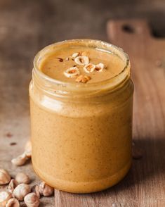 a jar filled with peanut butter sitting on top of a wooden table next to nuts