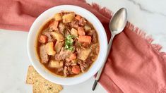 a white bowl filled with stew next to crackers and a pink towel on top of a table