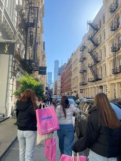 three women walking down the street with shopping bags in their hands and one carrying a pink bag