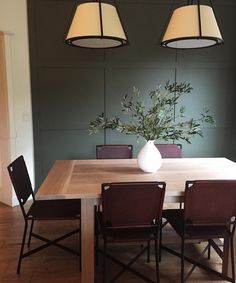 a dining room table with four chairs and a vase on the table in front of it