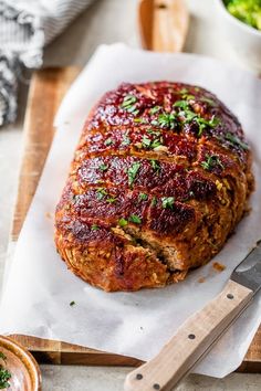 meatloaf with sauce and parsley on top sitting on a cutting board next to a bowl of broccoli