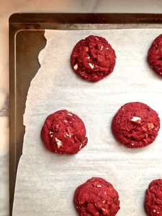 six red cookies sitting on top of a cookie sheet