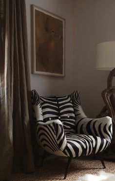 a zebra print chair sitting in front of a window next to a painting on the wall