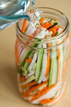 a glass jar filled with sliced up veggies and being drizzled with water