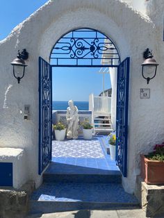 an archway leading to the ocean with statues on either side and potted plants in front