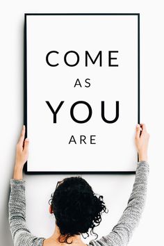 a woman holding up a poster with the words come as you are above her head