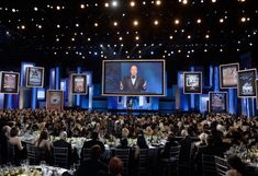 a large group of people sitting at tables in front of a screen with pictures on it