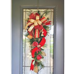 a christmas wreath hanging on the front door with red and gold ribbons, pine cones, holly berries and bells