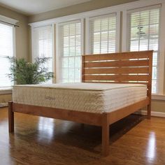 a wooden bed frame sitting on top of a hard wood floor next to a potted plant