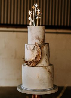 a three tiered white cake with gold stars and moon decorations on it's side