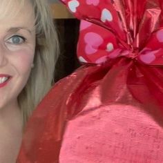 a woman with blonde hair and blue eyes holding a pink heart shaped bag in front of her face