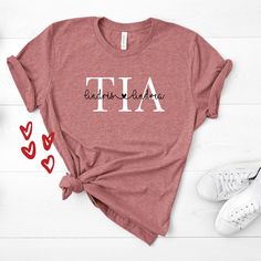 If you're looking for a personalized or custom auntie shirt for your favorite aunt then this Tia with the names of the nephews/nieces is perfect for you. Note: JUST ADD THE NAMES OF THE KIDS ON THE SPACE BELOW. You've now found the staple t-shirt of your wardrobe. It's made of a thicker, heavier cotton, but it's still soft and comfy. And the double stitching on the neckline and sleeves add more durability to what is sure to be a favorite! * 100% ring-spun cotton * Sport Grey is 90% ring-spun cot Custom Text Cotton Tops For Personalized Gift, Personalized Cotton T-shirt With Custom Text, Personalized Mother's Day Cotton Top, Personalized Name Print Short Sleeve Tops, Custom Text Cotton T-shirt For Personalized Gift, Custom Text Cotton T-shirt As Personalized Gift, Cotton Tops For Mother's Day, Personalized Casual Tops For Teacher Appreciation, Custom Print Cotton Tops For Personalized Gifts