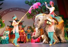 people are riding on the back of an elephant while others stand behind them in colorful costumes