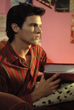 a young man sitting on a couch reading a book and looking at something in his hand