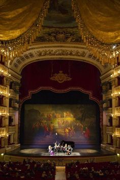 the stage is full of people and there are paintings on the wall above it, as well as an orchestra