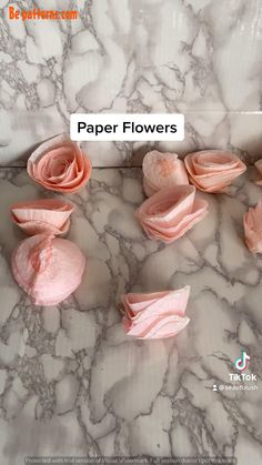 some pink flowers are on a marble counter top with the words paper flowers above them