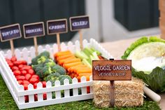 an assortment of vegetables on display at a vegetable garden stand with signs and straw bales